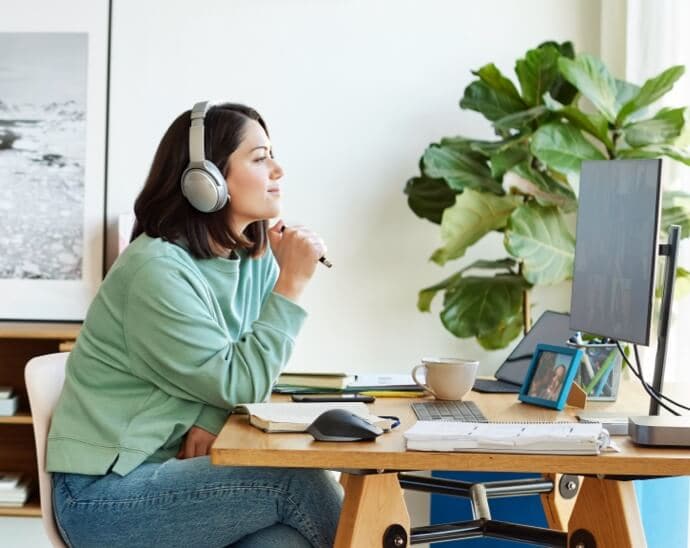 Kobieta w słuchawkach trzymająca długopis i patrząca na monitor komputera