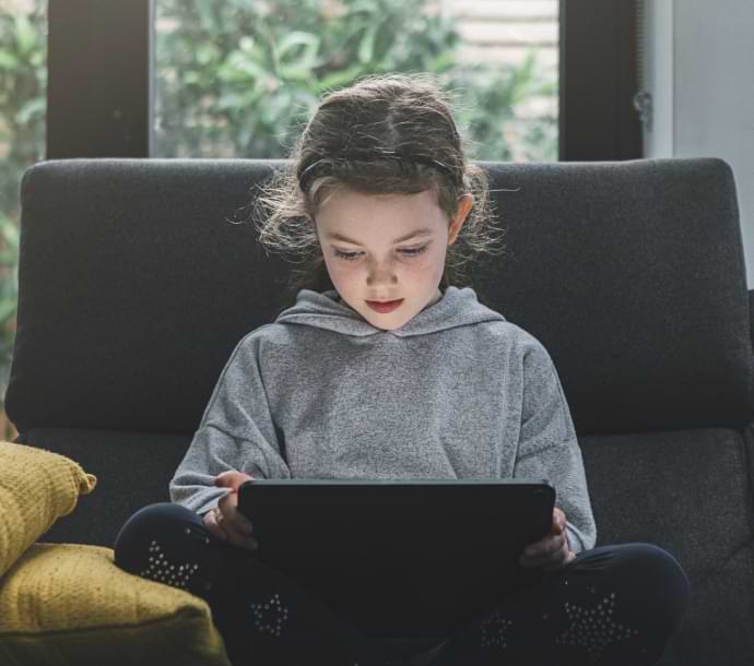 Dziewczyna na kanapie korzystająca z laptopa, na którym uruchamia się program Norton Family.