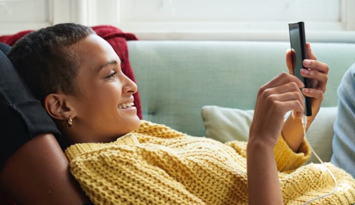 kobieta na kanapie patrząca na telefon komórkowy i uruchamiająca aplikację Norton 360 z dodatkiem AntiVirus Plus.