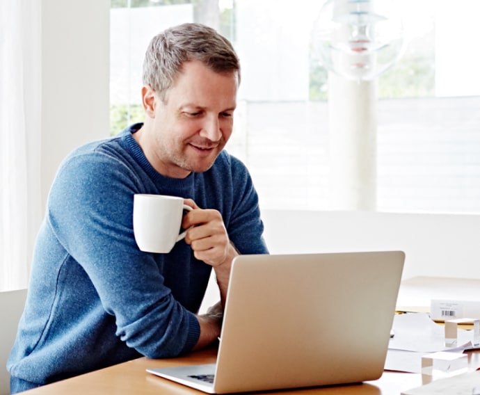 Mężczyzna w domu używający laptopa i pijący kawę.