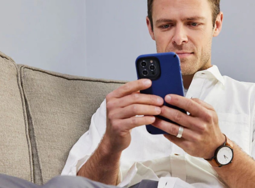Mężczyzna siedzi na kanapie i spogląda na telefon