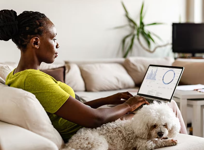 Kobieta siedzi i pracuje na laptopie w towarzystwie psa